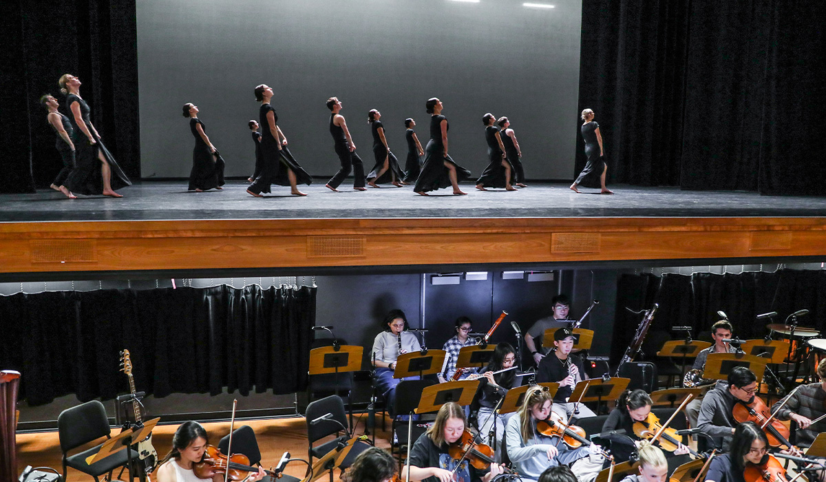 Chapman student dancers rehearse onstage while student musicians perform in the orchestra pit below.
