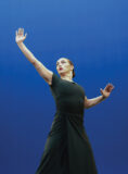 A Chapman student dancer in a long black dress reaches upward while performing beneath blue stage lighting.