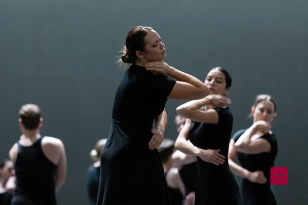 Chapman student dancers in long black dresses perform synchronized gestures under soft stage lighting.
