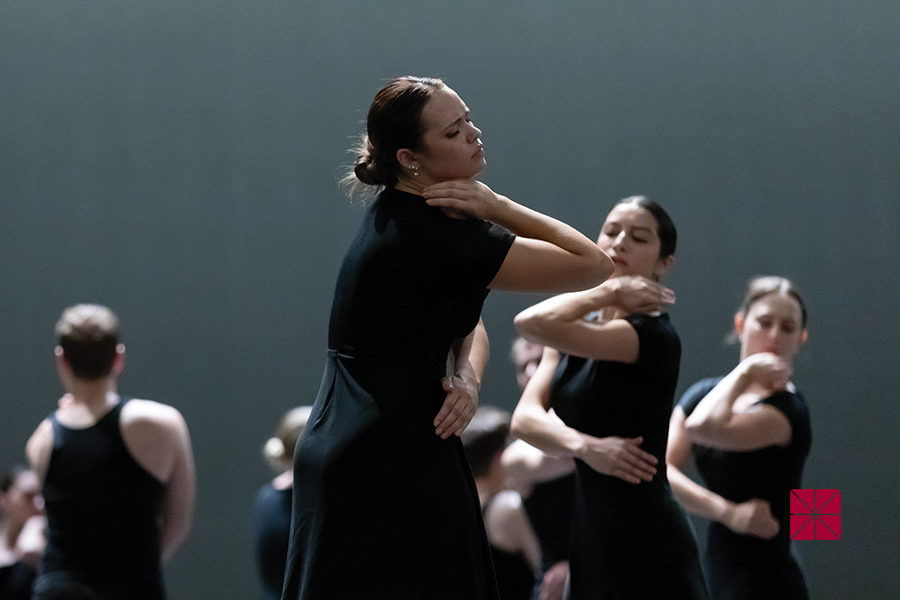 Chapman student dancers in long black dresses perform synchronized gestures under soft stage lighting.