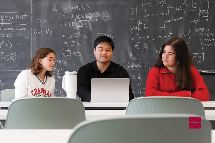 Three students sit in front of a black chalkboard.