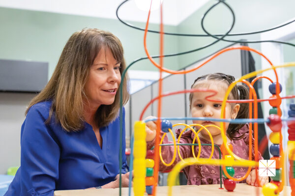 Laura Glynn sits with a toddler who plays with a toy.