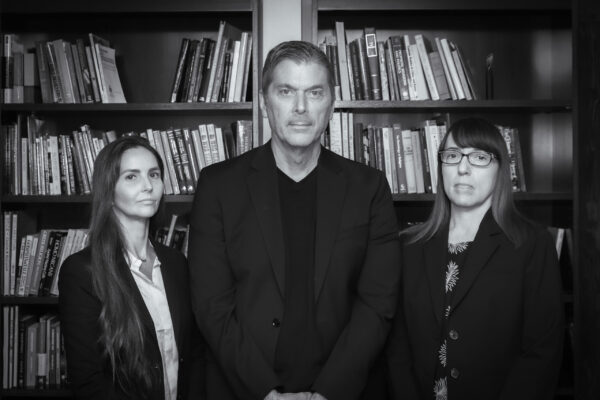 Ashley Kranjac, Christopher Bader, and Ann Gordon stand in front of bookshelves in a black-and-white portrait.
