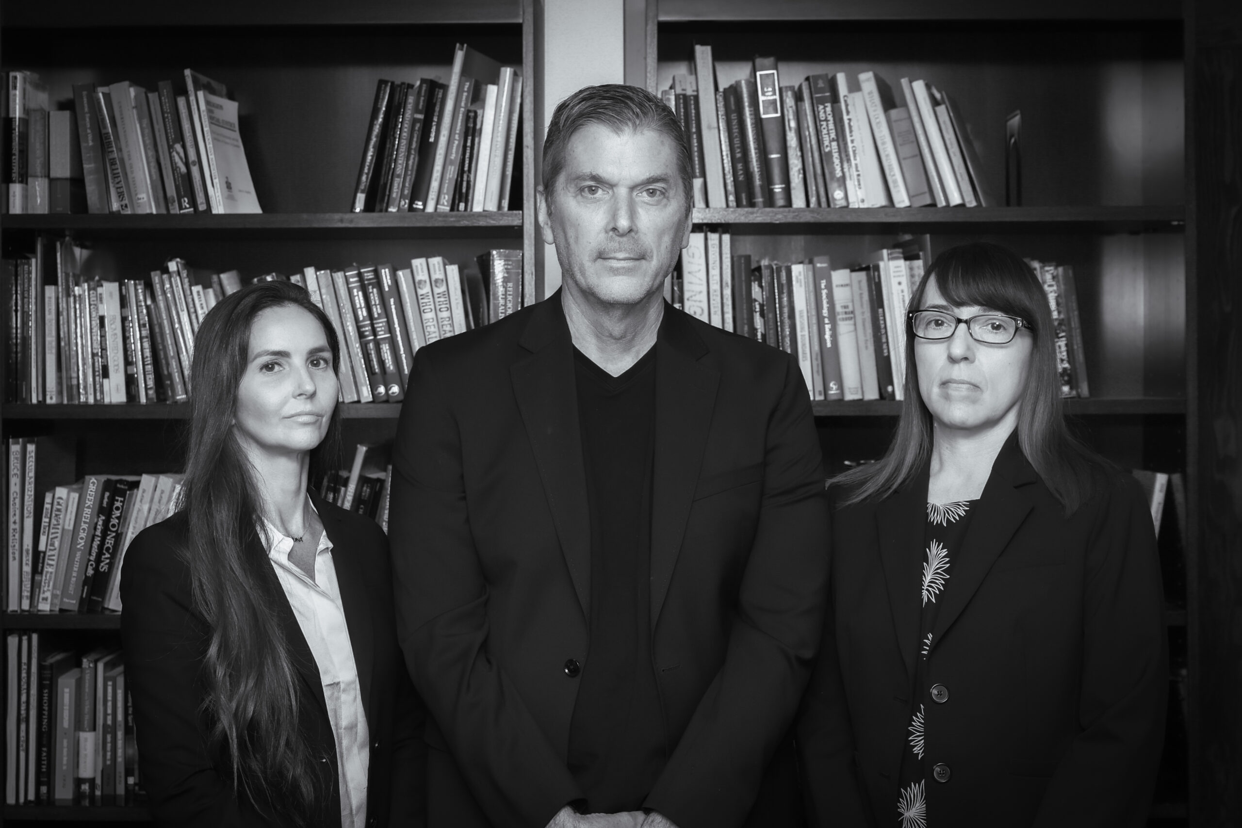 Ashley Kranjac, Christopher Bader, and Ann Gordon stand in front of bookshelves in a black-and-white portrait.